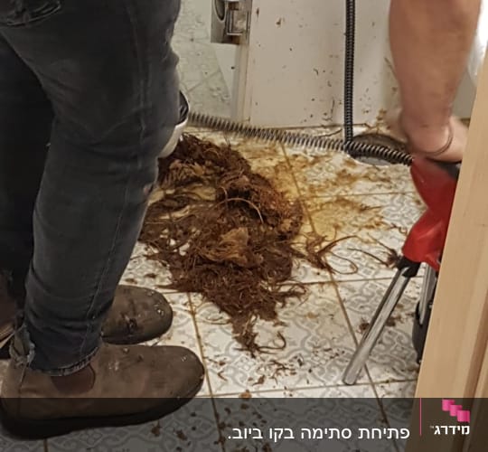 אינסטלטור משתמש במכשיר לפתיחת סתימות בצנרת